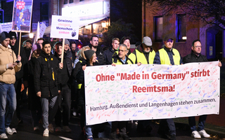 Viele Menschen laufen bei einer Demonstration auf der Straße. Die Menschen in der ersten Reihe tragen ein Banner mit der Aufschrift "Ohne Made in Germany stirbt Reemstma"